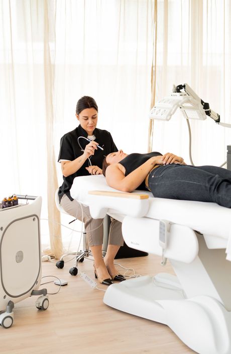 Une esthéticienne maquille une cliente allongée sur une table de soins dans un studio lumineux