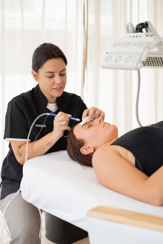 Esthéticienne appliquant un soin du visage à une cliente allongée dans une cabine de spa lumineuse