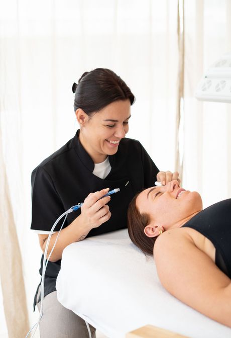 Un thérapeute souriant tient un appareil en forme de stylo près d’un client allongé sur une table de soins