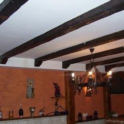 Comedor rústico con vigas oscuras a la vista, paredes naranjas y una lámpara de araña colgante.