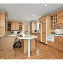 Amplia cocina de madera clara con isla central, refrigerador de acero inoxidable, encimeras blancas y pisos de madera noble.