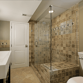 Ducha a ras de suelo con mampara de cristal y azulejos en un baño de color beige.