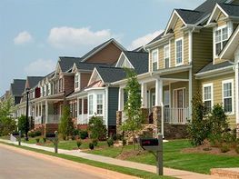 Hilera de coloridas casas suburbanas a lo largo de una tranquila calle residencial con céspedes bien cuidados y acera.