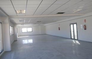 Habitación blanca vacía con suelo brillante, ventanas y puertas dobles de cristal.