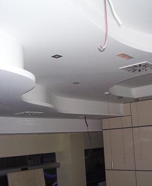 Techo curvo blanco con luces empotradas y cables colgantes en una habitación interior sin terminar.