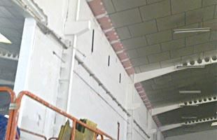 Interior de una obra en construcción con una pared de ladrillo blanco, barandilla de andamio y vigas en el techo.