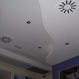Techo con luces empotradas y un panel blanco ondulado sobre la esquina de una habitación con una pared azul.
