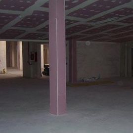 Interior vacío y sin terminar con una columna de soporte rosa y baldosas de techo estampadas.