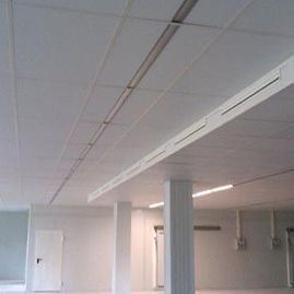 Interior de oficina blanco vacío con falso techo, luces fluorescentes, columnas y una puerta cerrada.