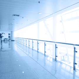 Pasillo luminoso y vacío, similar al de un aeropuerto, con barandillas de cristal y suelo azul brillante.
