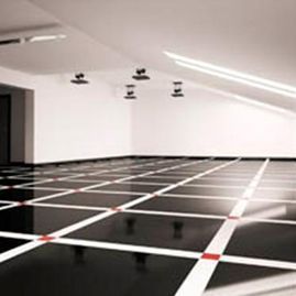 Habitación blanca minimalista con suelo de cuadrícula en blanco y negro y pequeños dispositivos montados en el techo.