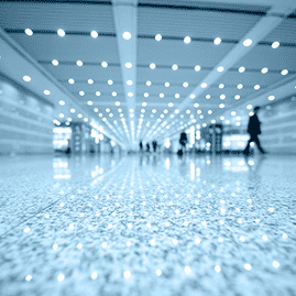 Terminal de aeropuerto de color azul brillante con viajeros borrosos y reflejos de las luces del techo en el suelo.