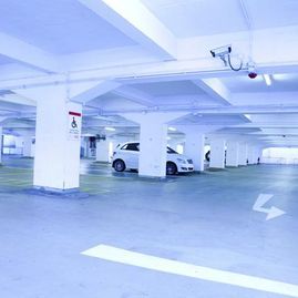 Garaje cubierto vacío con pilares blancos y algunos coches aparcados.