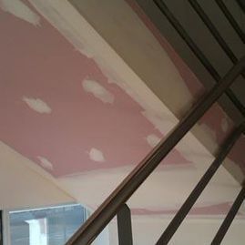 Techo rosa con manchas blancas que parecen nubes y vigas metálicas diagonales en una escalera interior.