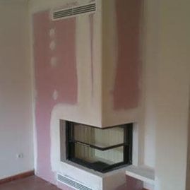 Chimenea de esquina interior con paredes rosas sin acabado y frontal de cristal negro.
