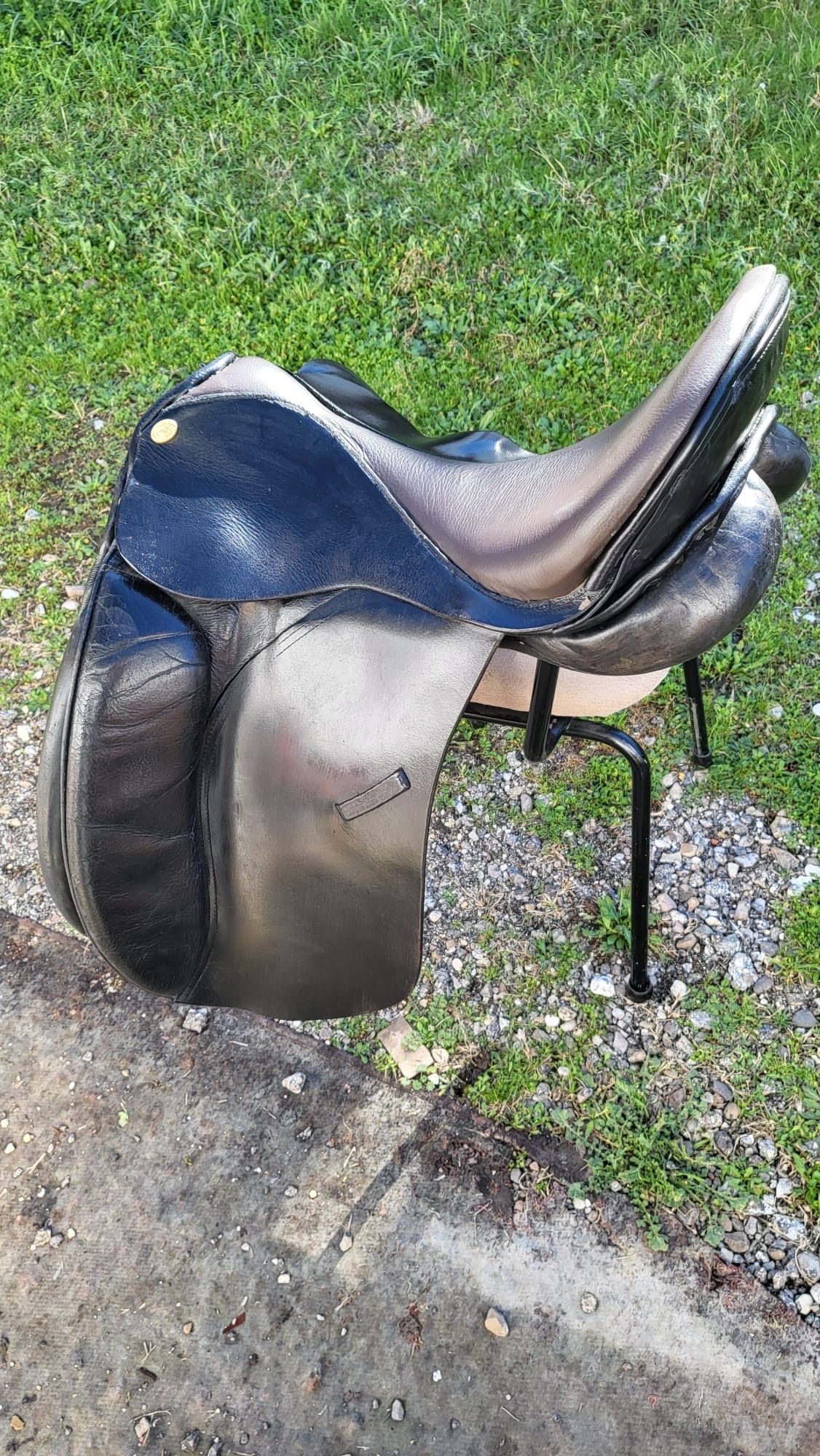 Silla de montar de cuero marrón sobre un soporte metálico, junto al borde de una carretera con césped