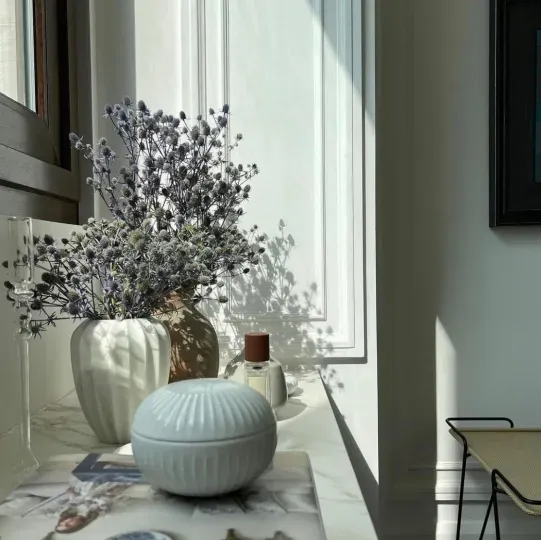 Un jarrón con flores moradas se encuentra en el alféizar de una ventana.