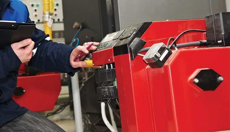 Une personne manipule une machine industrielle rouge à l'aide d'une télécommande dans un atelier.
