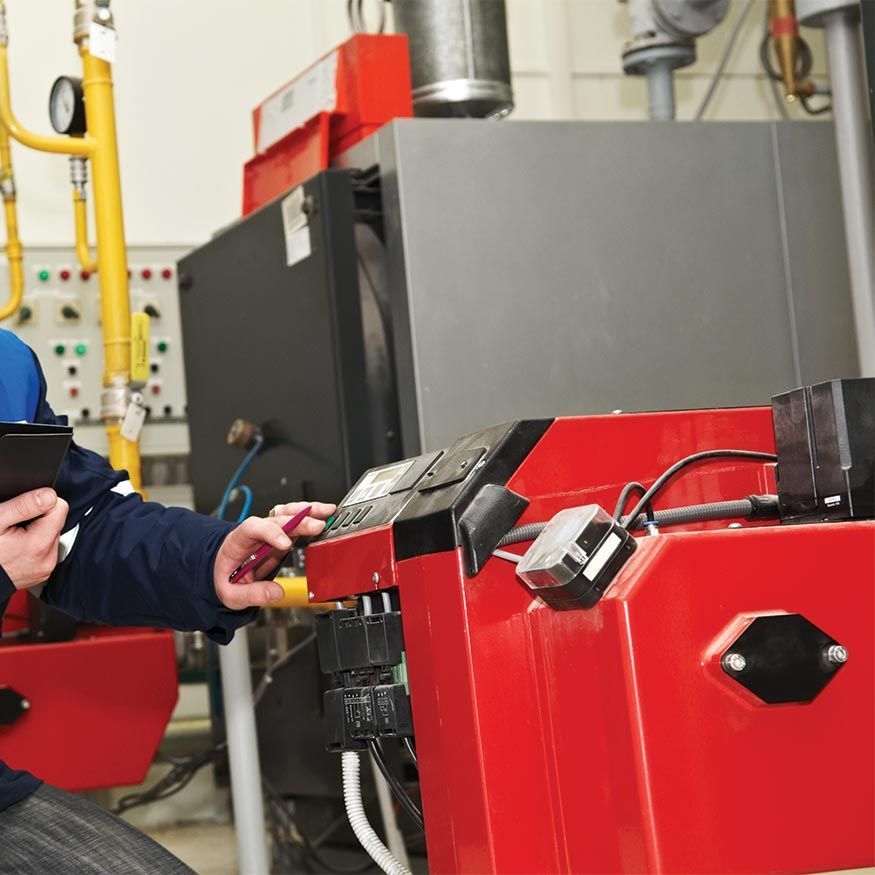Un technicien ajuste les commandes d'une machine industrielle rouge dans un atelier