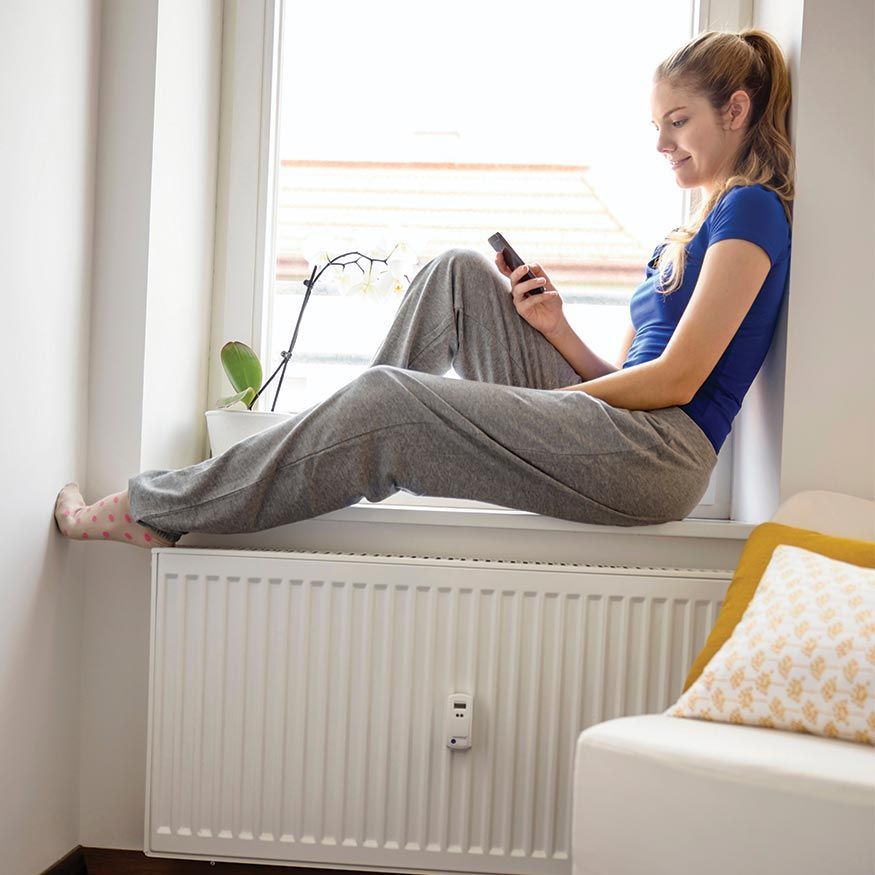 Une femme assise sur le rebord d'une fenêtre, souriant à son téléphone dans une pièce lumineuse