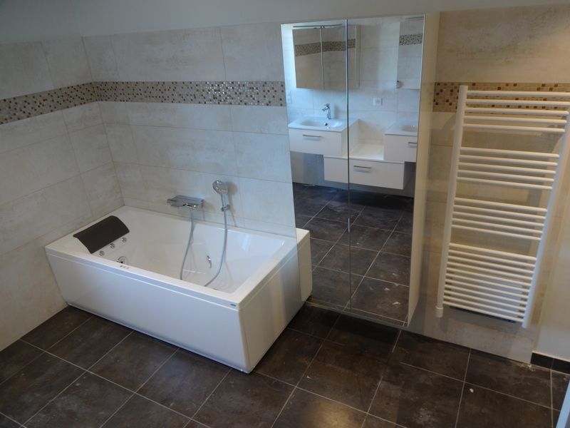 Salle de bains moderne avec baignoire blanche, sol carrelé foncé, douche en verre et sèche-serviettes