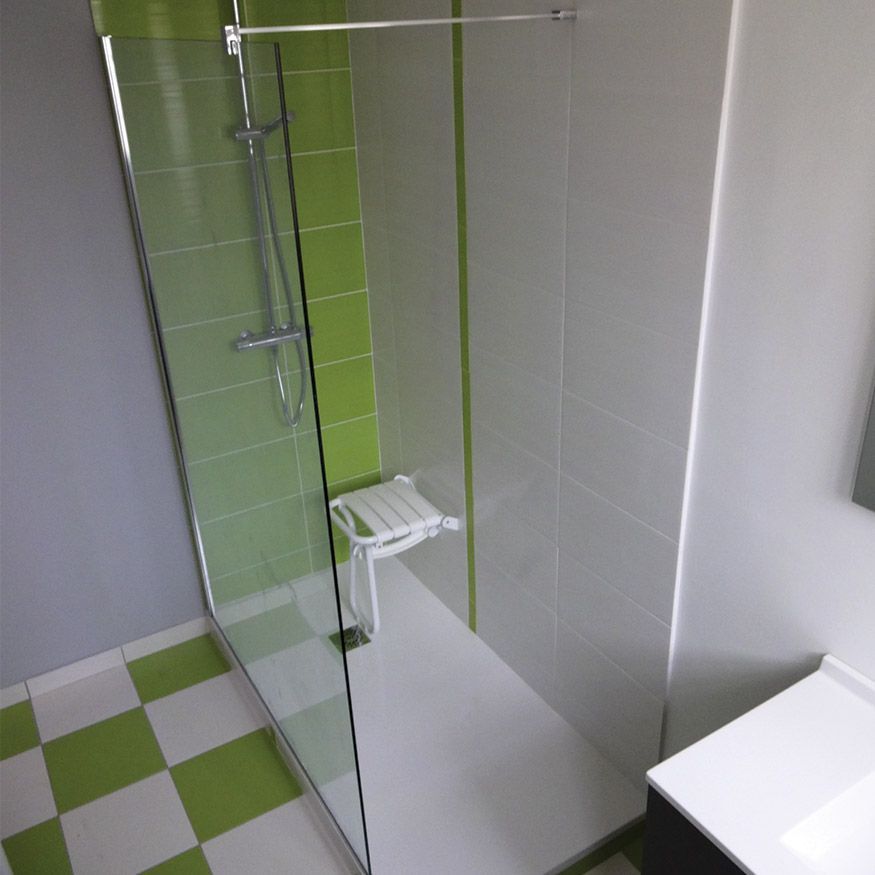 Douche moderne avec porte en verre, murs blancs, sol carrelé vert et blanc et frise décorative.