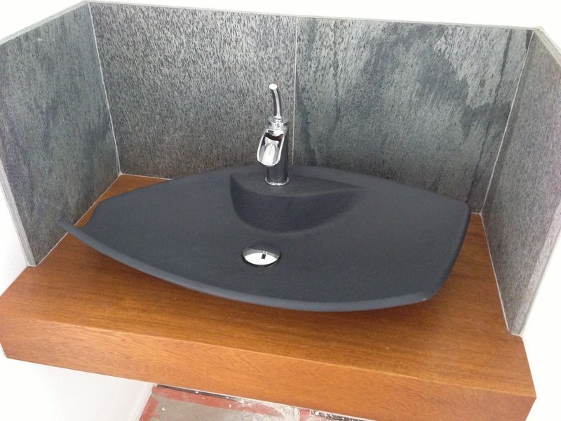 Petit lavabo noir avec robinet sur un meuble-lavabo en bois, devant des murs carrelés gris.