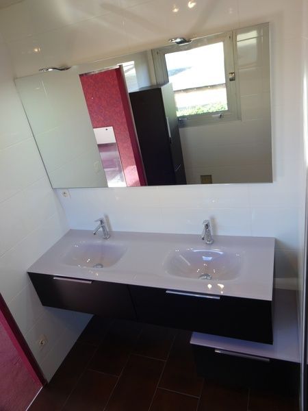 Meuble-lavabo moderne avec double vasque, grand miroir, murs blancs et sol carrelé foncé.