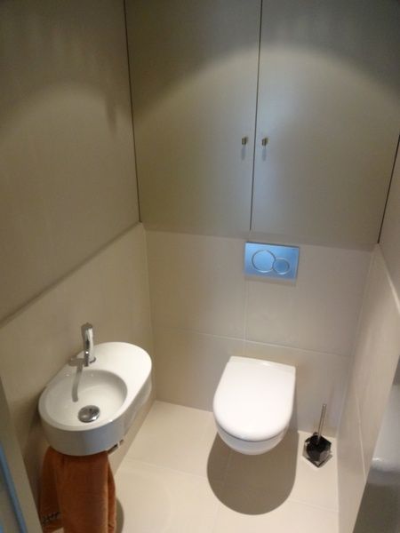 Petite salle de bains avec toilettes suspendues, lavabo et portes de placard au-dessus.