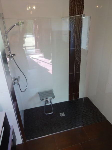 Douche à l'italienne accessible avec paroi en verre, pommeau de douche amovible et sol carrelé noir.
