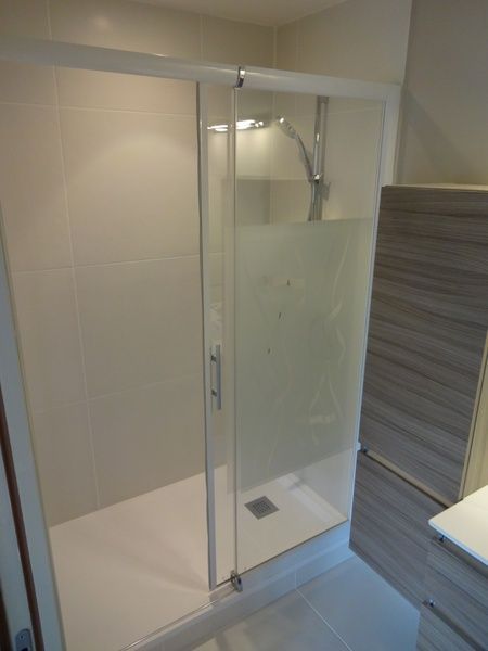 Douche à l'italienne en verre avec carrelage blanc, paroi dépolie et robinetterie chromée dans une salle de bain moderne