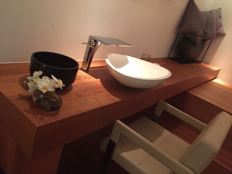 Meuble-lavabo moderne avec comptoir en bois, lavabo blanc, vasque noire, robinet et chaise beige