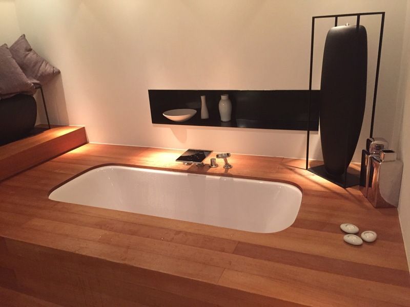 Salle de bains moderne avec baignoire à débordement blanche, habillage en bois, bougies et décoration minimaliste