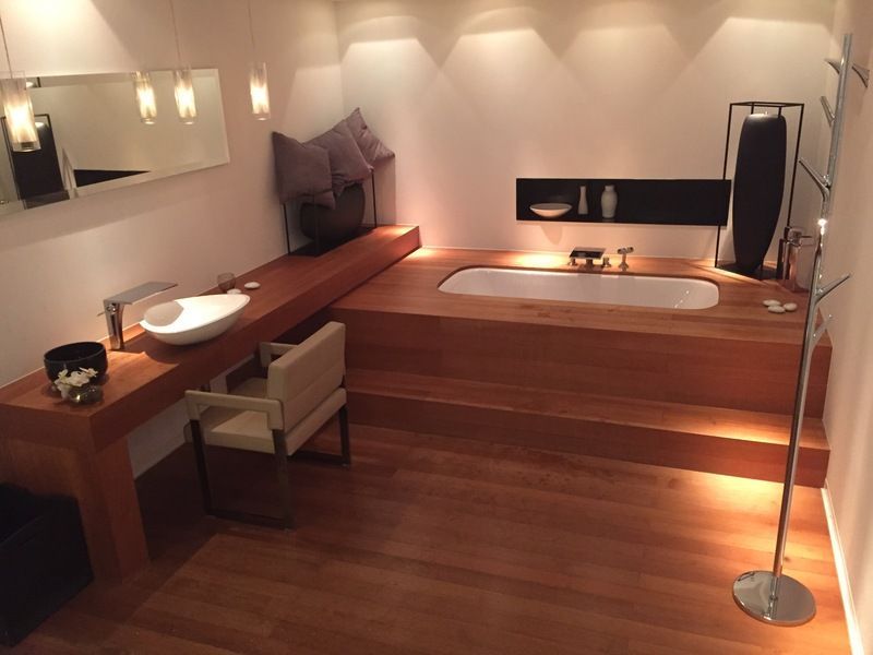 Salle de soins spa moderne avec baignoire surélevée en bois, lavabo, banquette et éclairage doux et chaleureux