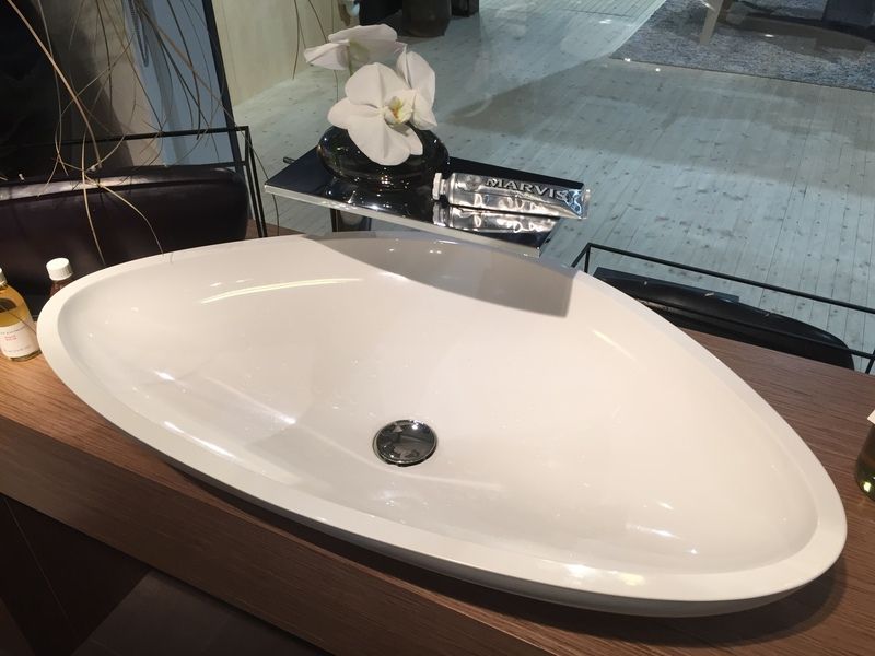 Lavabo ovale blanc avec bonde chromée sur un plan de travail foncé, à côté d'une fleur blanche.