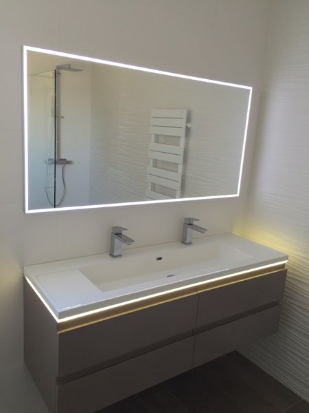 Salle de bains moderne avec meuble-lavabo suspendu, miroir éclairé et douche murale visible dans le reflet