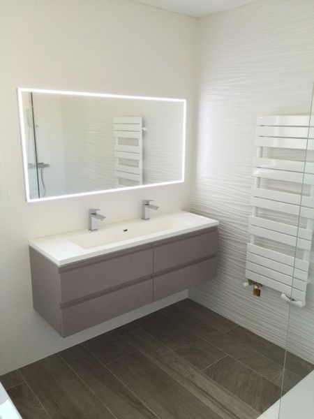 Salle de bains moderne avec meuble-lavabo double suspendu, grand miroir et sèche-serviettes blanc sur un sol gris imitation bois.