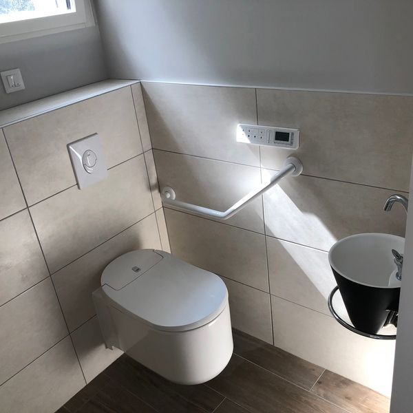 Salle de bain accessible avec toilettes suspendues, barre d'appui et lavabo