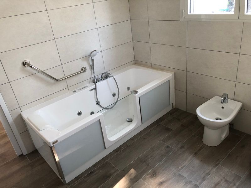 Salle de bain accessible avec baignoire, siège de transfert intégré, barres d'appui murales et toilettes bidet
