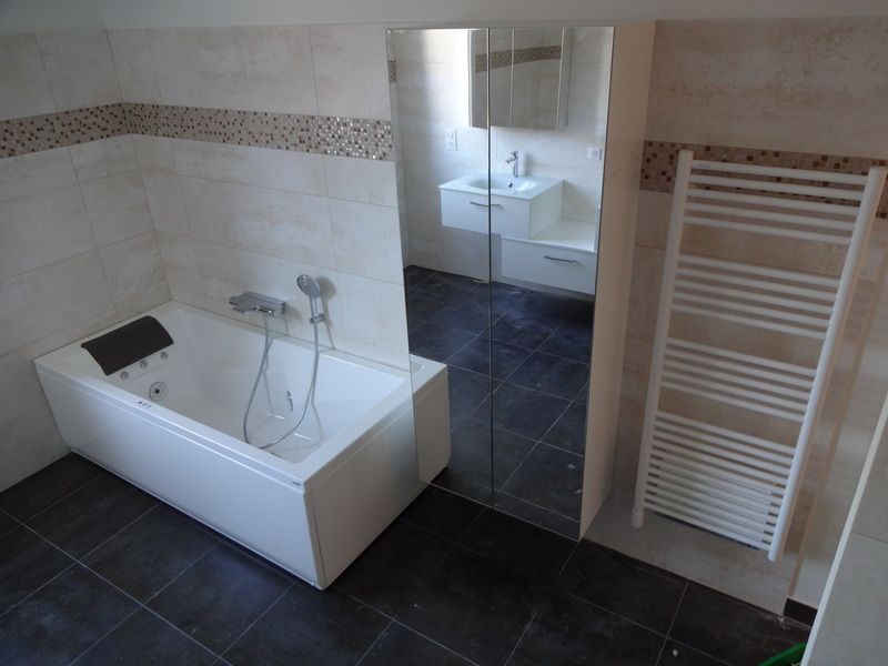 Salle de bains avec baignoire blanche, sol carrelé foncé, lavabo et sèche-serviettes à côté d'une armoire à miroir.