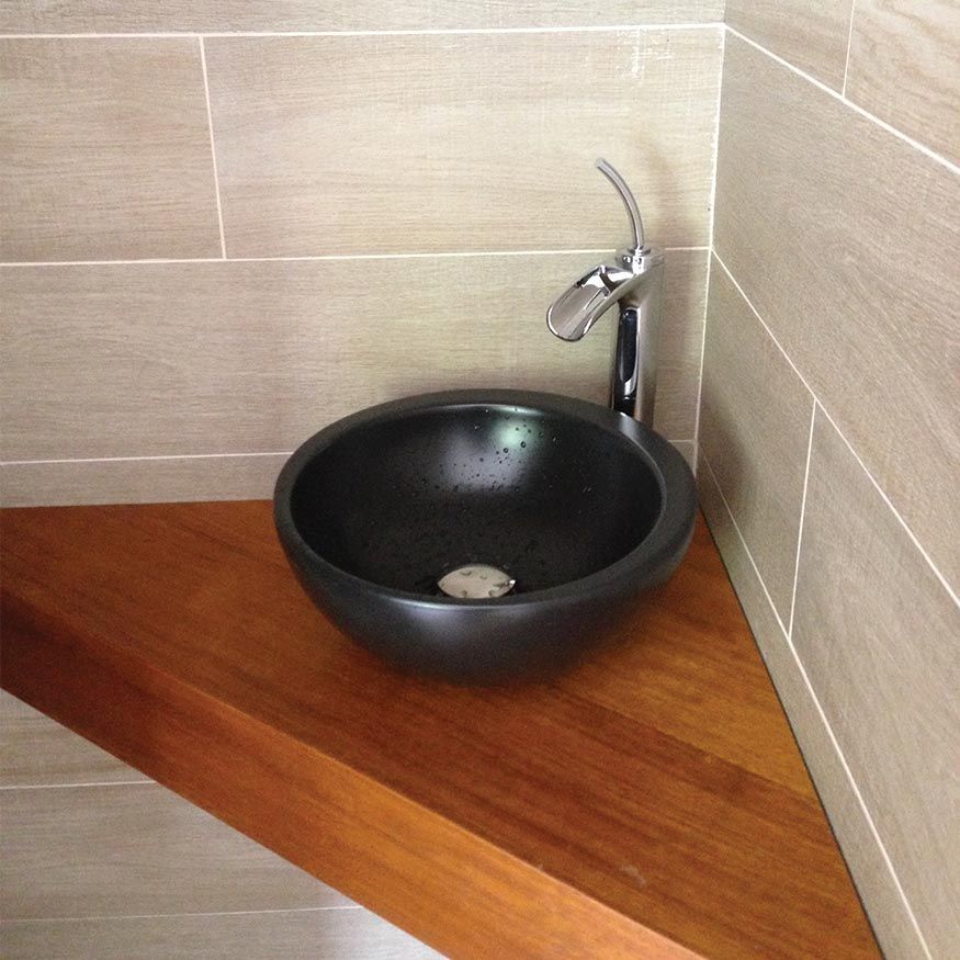 Lavabo rond noir avec robinet chromé sur un comptoir en bois dans un coin lavabo carrelé