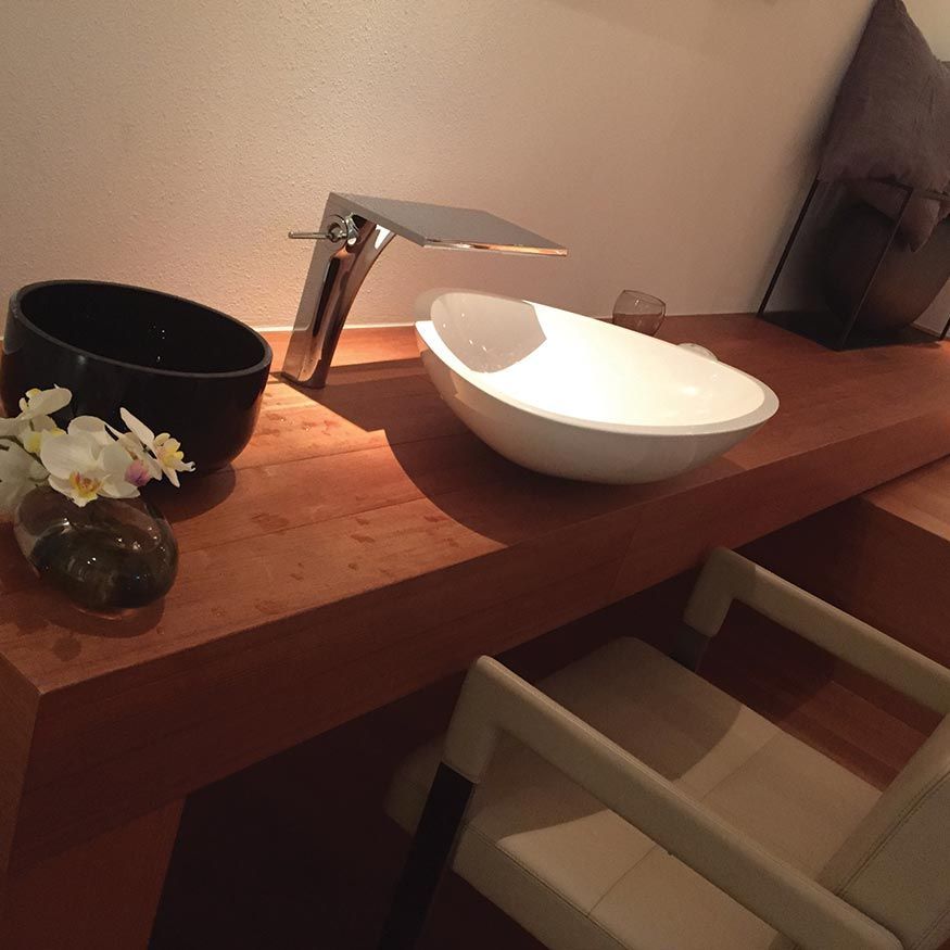 Meuble-lavabo moderne avec vasque, robinet chromé, bol noir et petit arrangement floral.