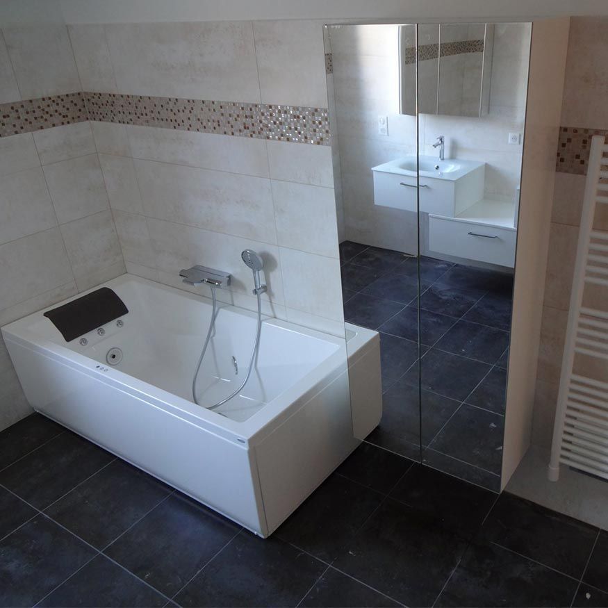 Salle de bains moderne avec baignoire blanche, paroi de douche en verre et sol carrelé foncé.