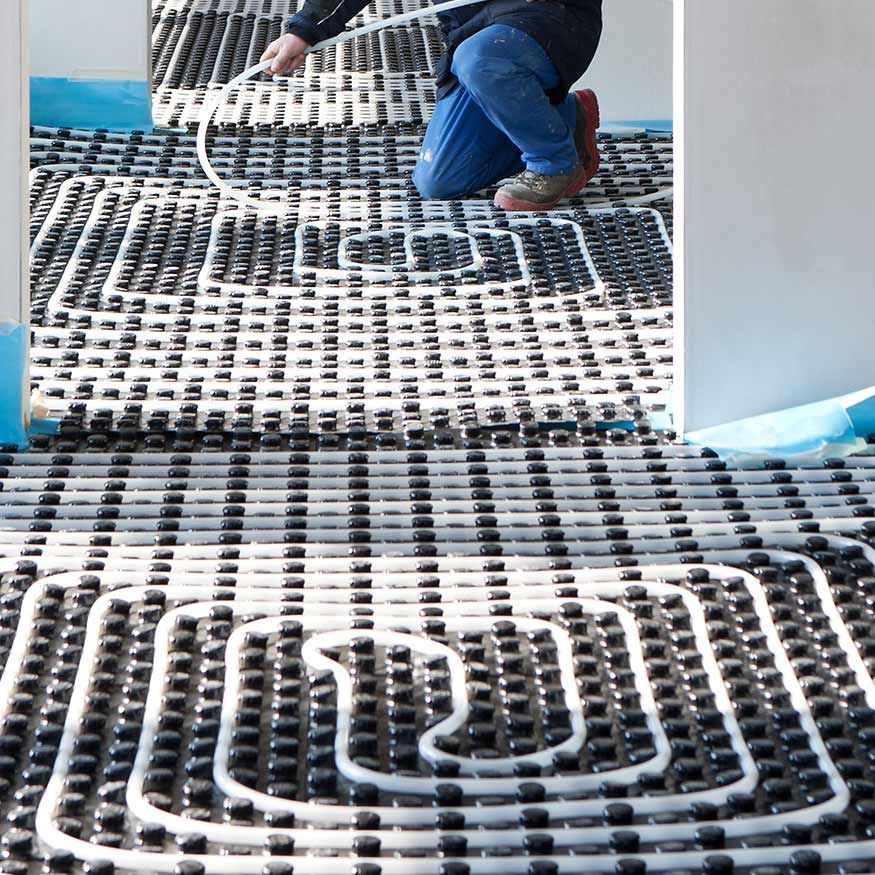 Ouvrier installant des tubes blancs pour un chauffage au sol radiant sur une surface au sol