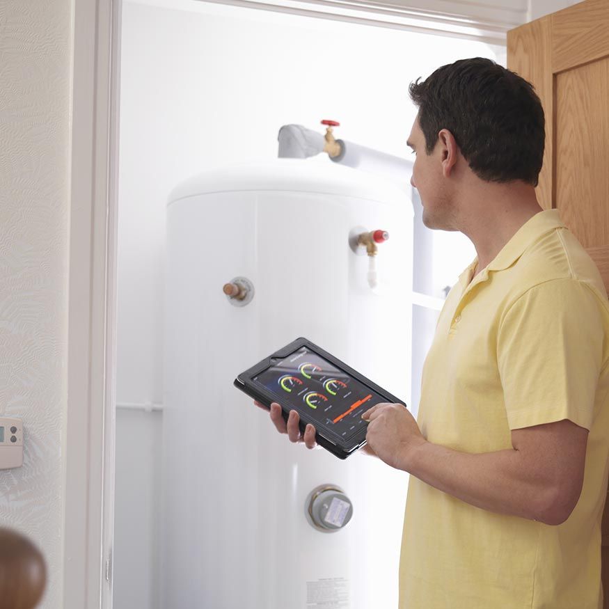 Un homme tenant une tablette inspecte un chauffe-eau blanc dans une buanderie lumineuse.