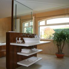 Salle de bains moderne avec vasque, meuble-lavabo en bois, miroir et grande fenêtre donnant sur la verdure.