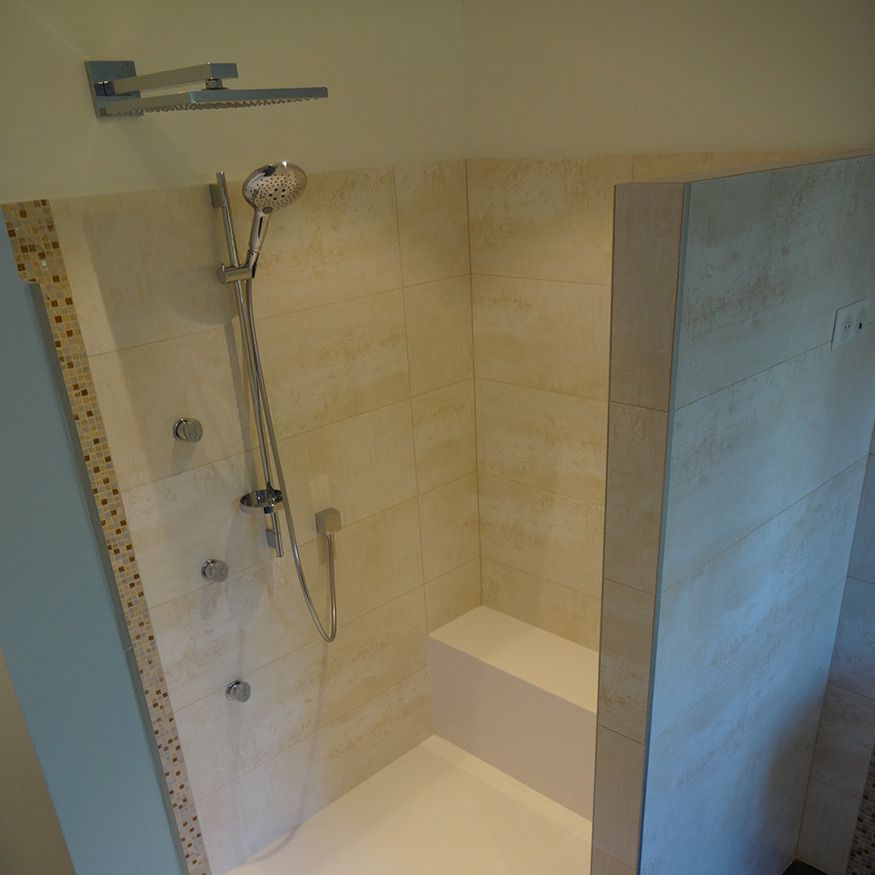 Cabine de douche accessible avec banc intégré, pommeau de douche chromé et murs carrelés beiges.