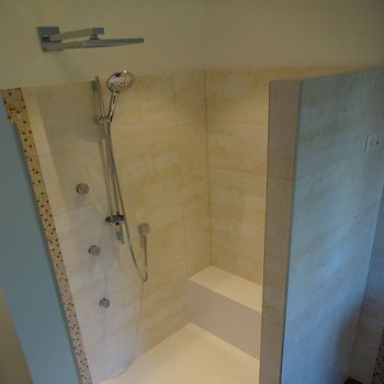 Cabine de douche accessible avec banc intégré, pommeau de douche chromé et murs carrelés beiges.