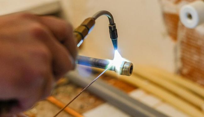 Main utilisant un chalumeau pour chauffer un tube métallique dans un atelier, avec une flamme vive et des étincelles.