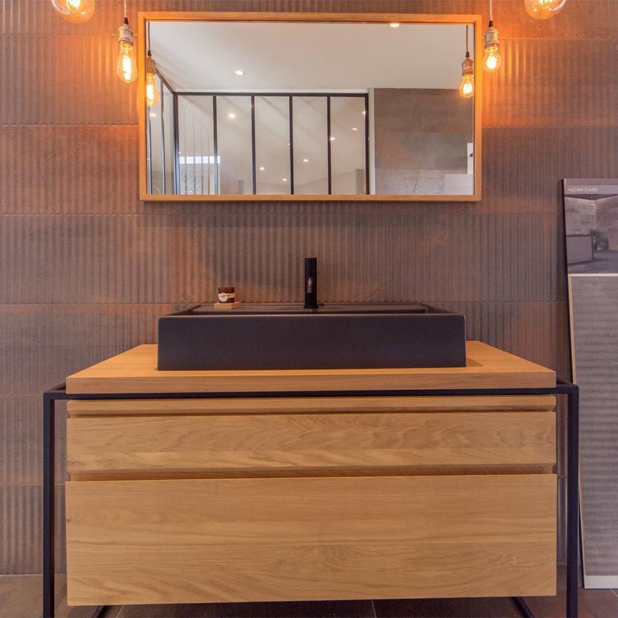 Meuble-lavabo moderne avec armoire en bois, lavabo noir et miroir rectangulaire sur un mur carrelé avec appliques murales à l'éclairage chaleureux.